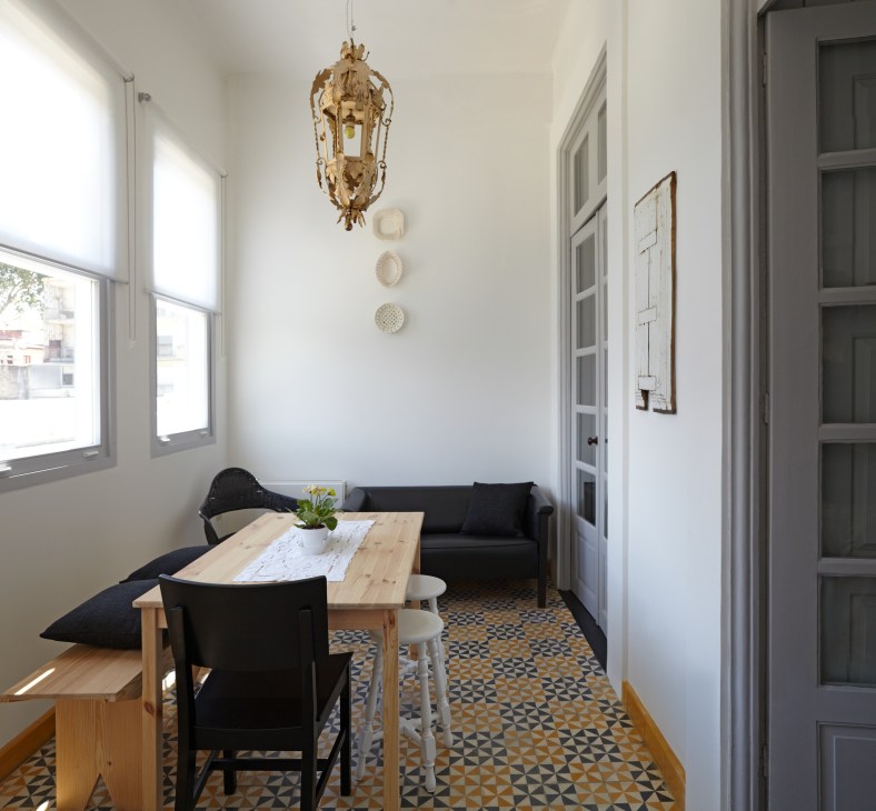 Minimalist hotel room with wooden table, black chairs, black sofa, and geometric patterned floor.