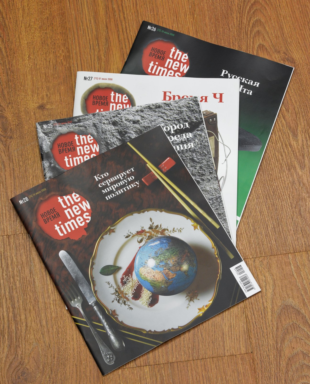 Four issues of The New Times magazine displayed on a wooden surface, showing the publication's distinctive red circular logo and various cover designs.