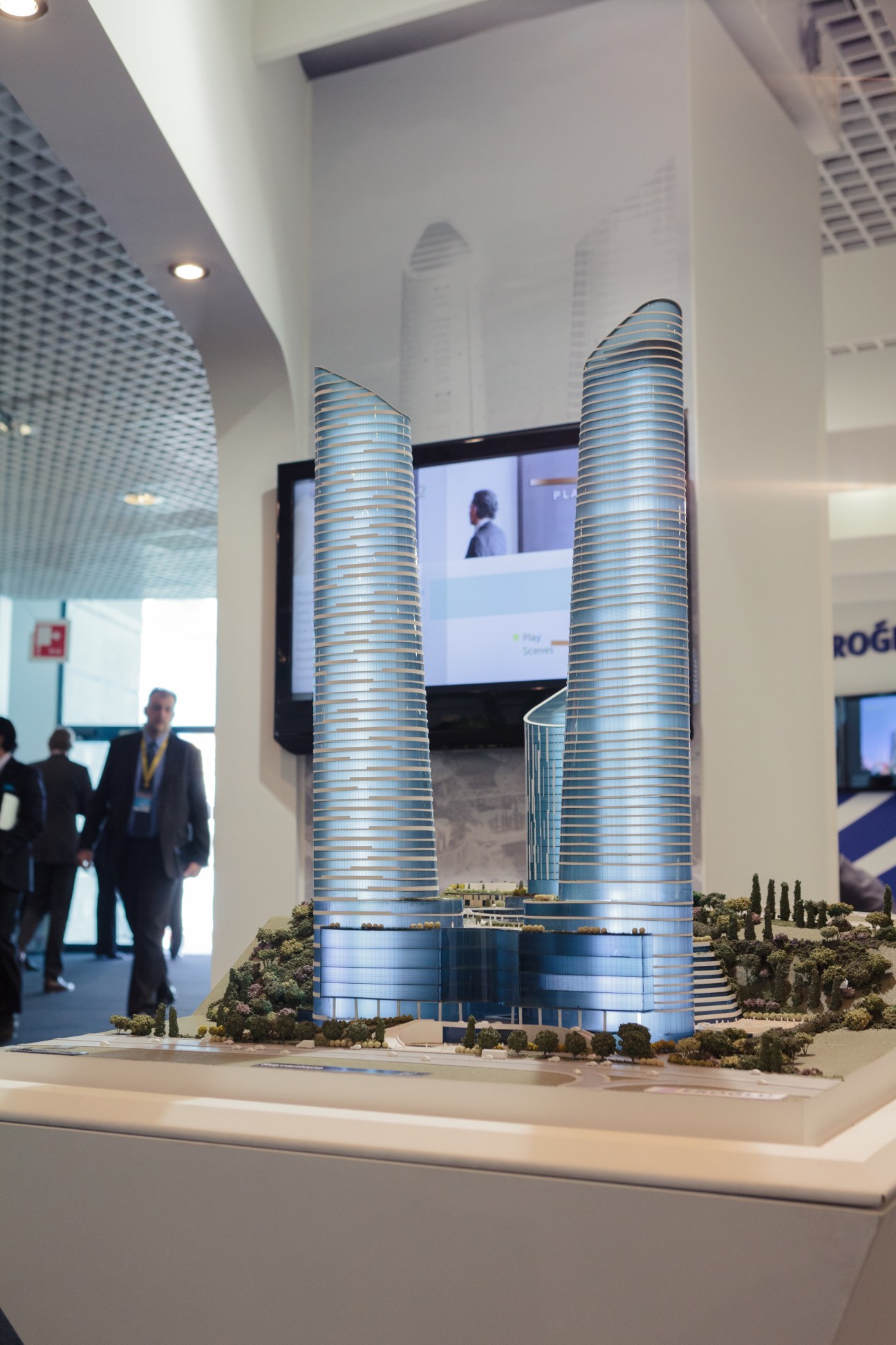 Architectural model of two curved tower buildings with blue striping displayed at a MIPIM booth.