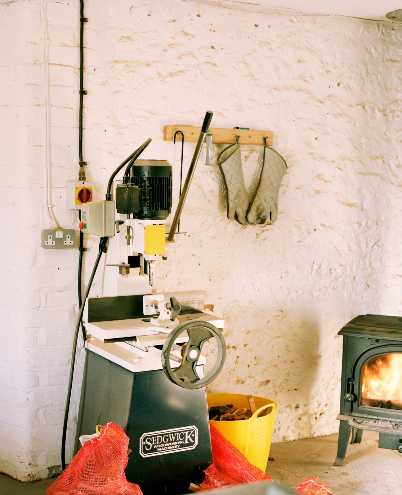 A Sedgwick woodworking machine mounted on a white brick wall in a workshop with hand tools and a wood storage rack.