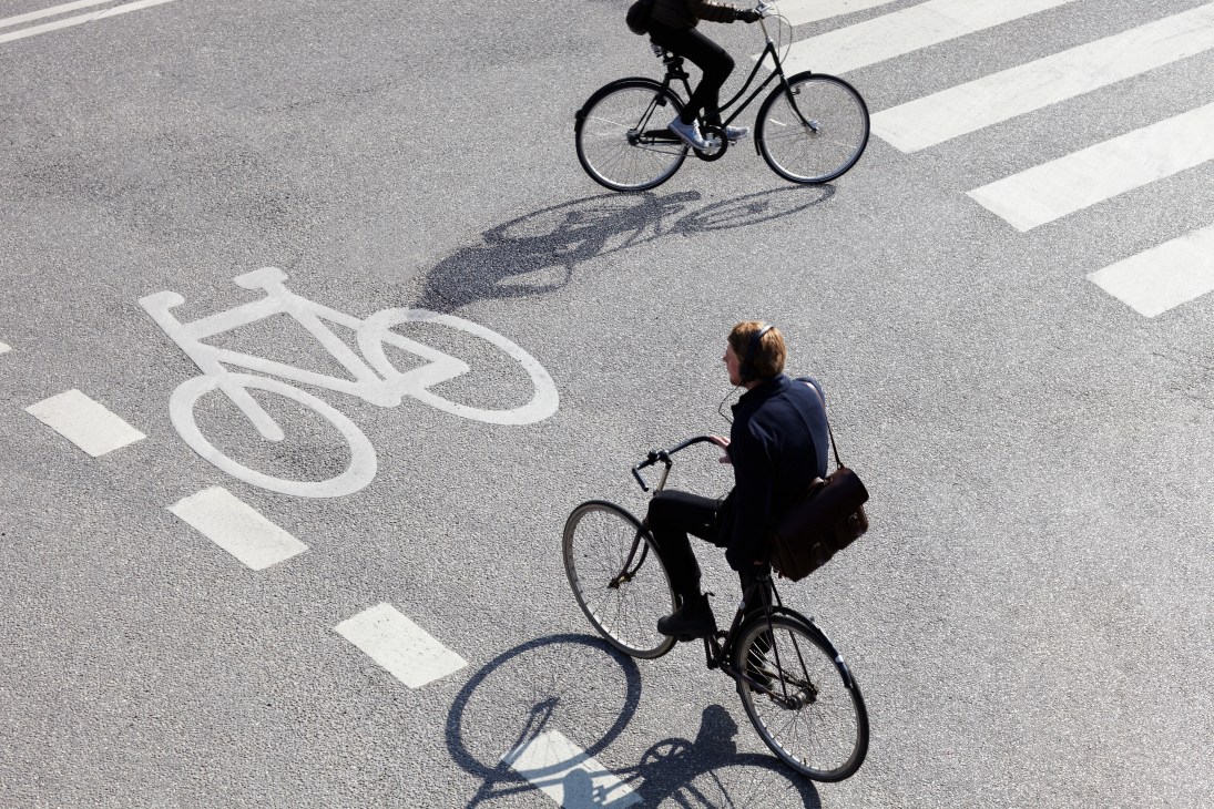 Two cyclists ride across a zebra crossing marked with a bike lane symbol in Copenhagen.
