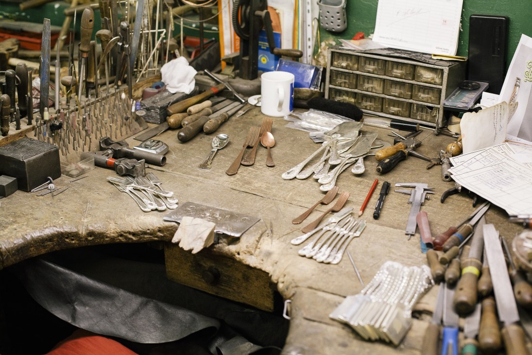 Silverware craftsman's workbench with hand tools, metal cutlery pieces, and wooden-handled implements at Jarosinski & Vaugoin atelier.