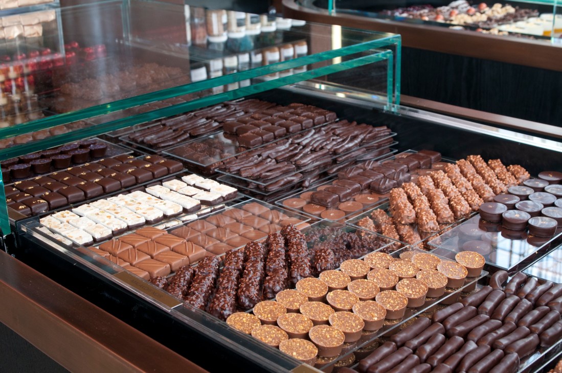 Display case with various chocolate confections and pastries arranged in rows behind glass.