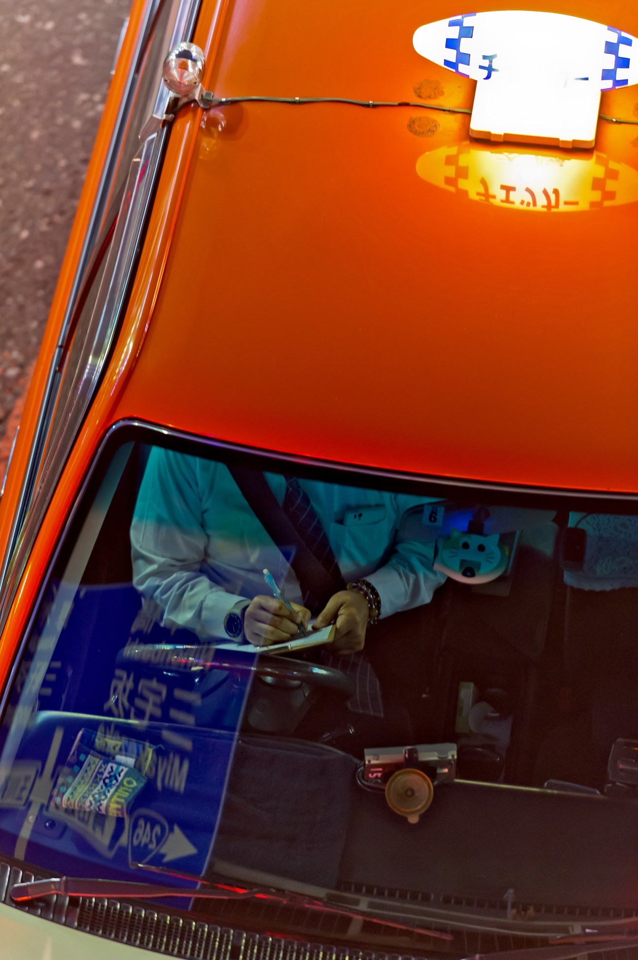 Tokyo taxi driver in orange cab writing in logbook to record trip and fare details.