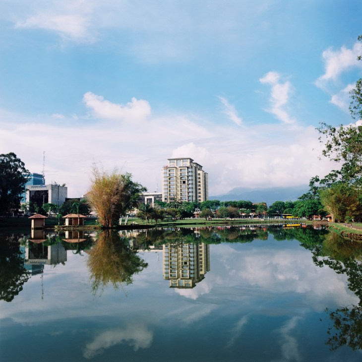 Modern apartment building reflected in still water at Parque La Sabana in San José.