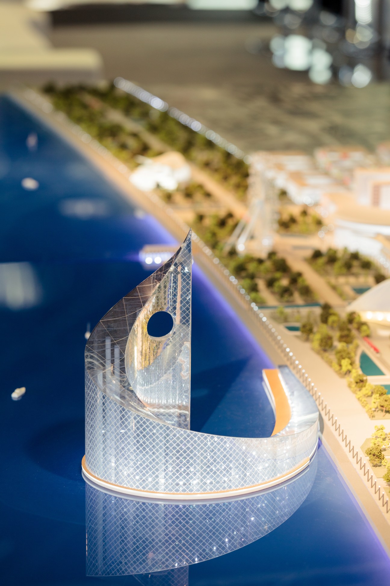 Architectural model detail of Foster + Partners' White City project in Baku showing a curved white structure with lattice pattern and blue water feature.