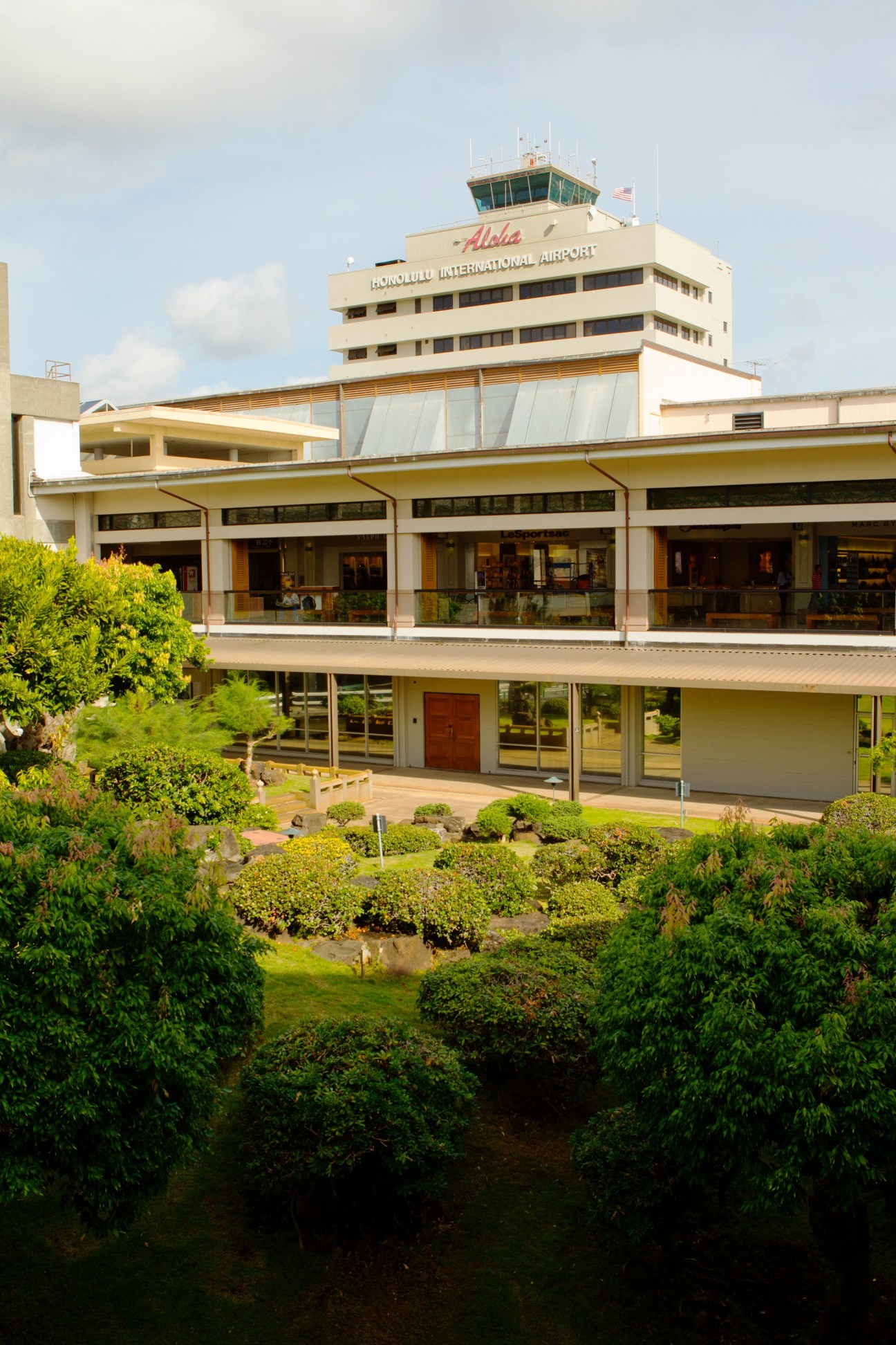 Honolulu International Airport terminal building with control tower, modernist concrete and wood architecture surrounded by tropical landscaping.