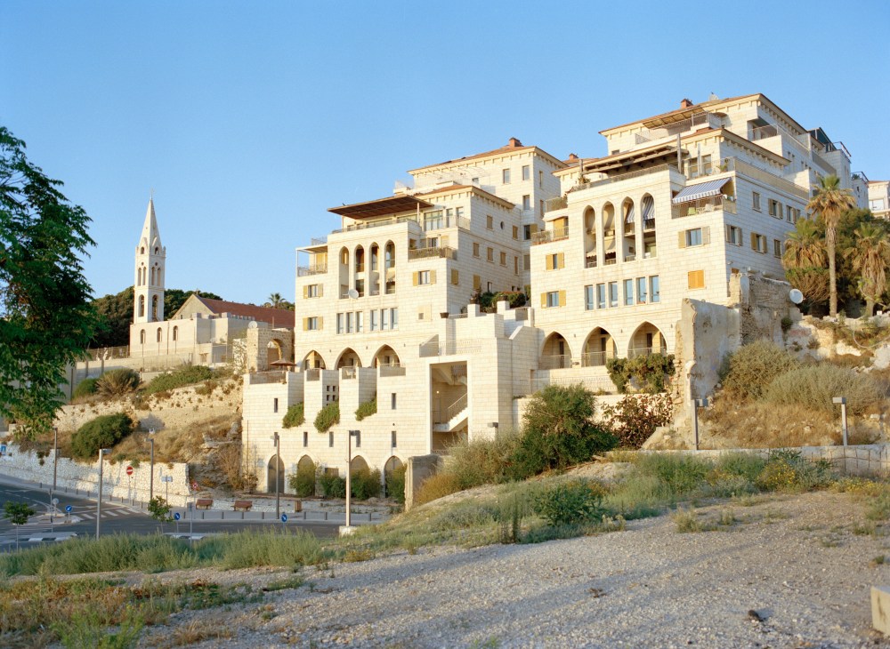 Modern stone apartment buildings with arched windows built on hillside in ancient Jaffa with church in background.
