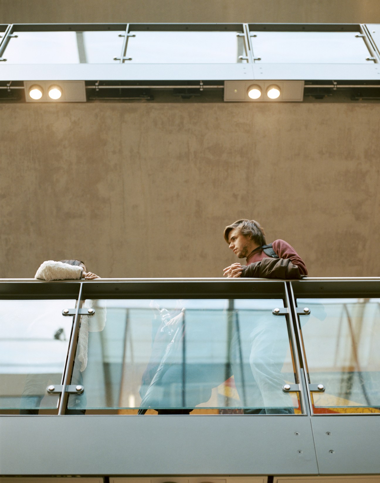 Student leaning on a glass and metal railing overlooking the interior atrium of Central Saint Martins' Granary Building.