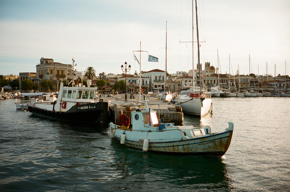 Traditional fishing boats moored in Aegina's main harbour with neo-classical waterfront buildings behind.