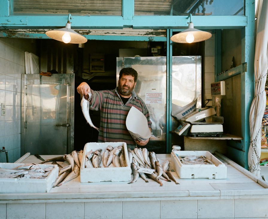 Fish vendor displaying fresh catch at Aegina's main fish market stall with turquoise storefront.