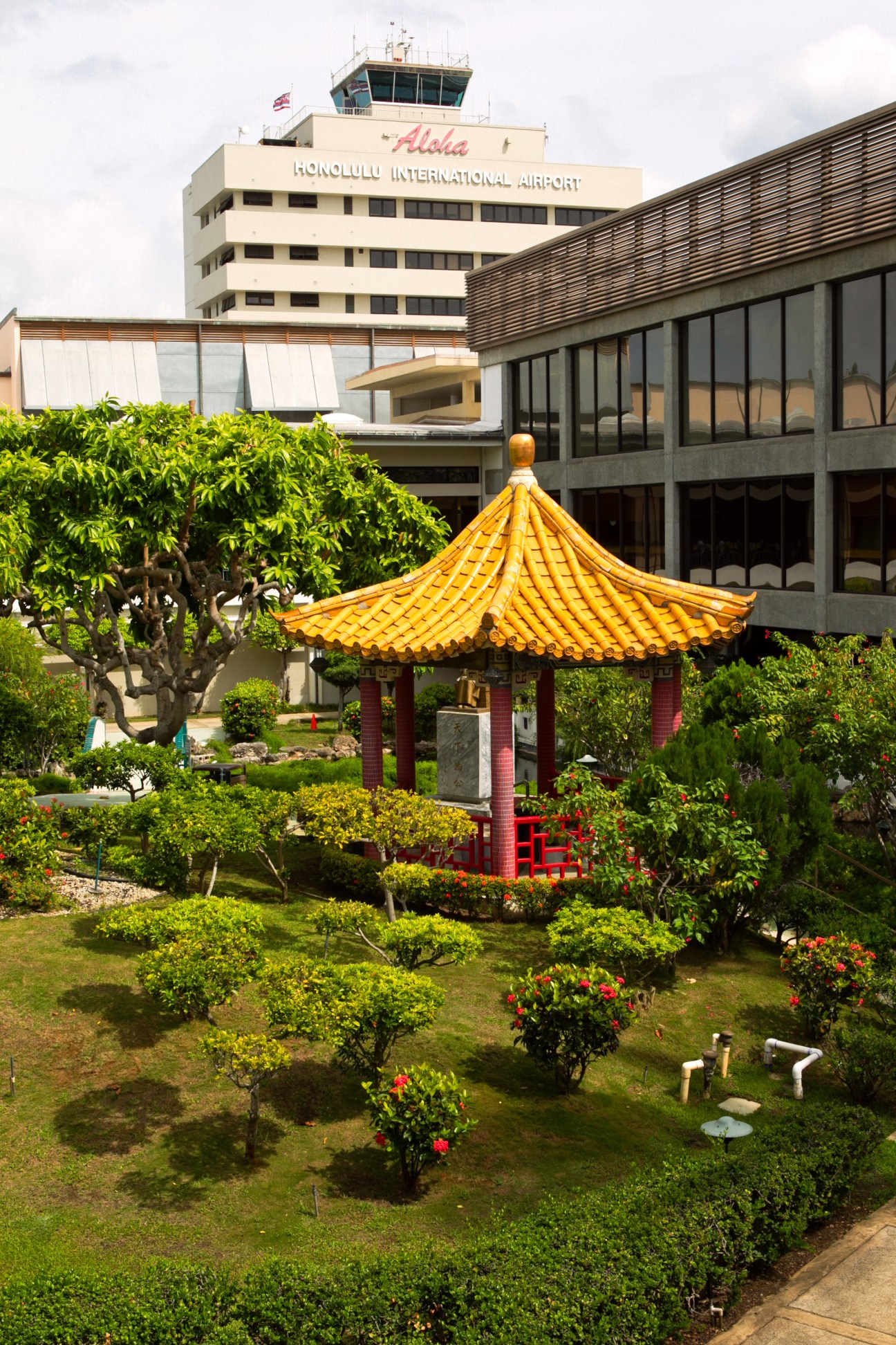 Honolulu International Airport control tower with Japanese garden pavilion featuring golden roof and surrounding landscaping in foreground.