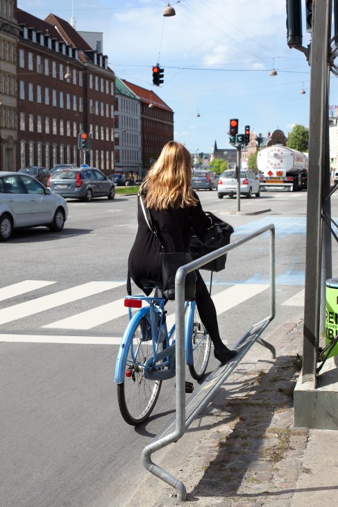 Woman in black jacket waiting at a traffic light on a blue bicycle in Copenhagen
