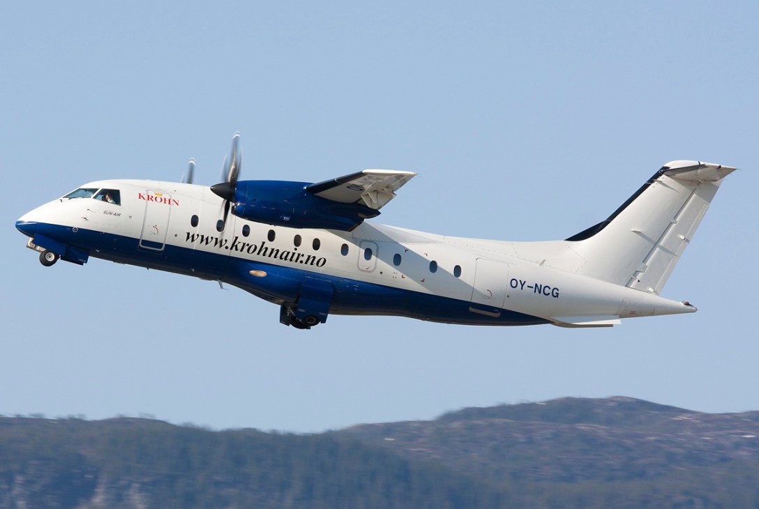 Krohn Air Dornier 328 turboprop aircraft in flight with blue and white livery against clear sky.