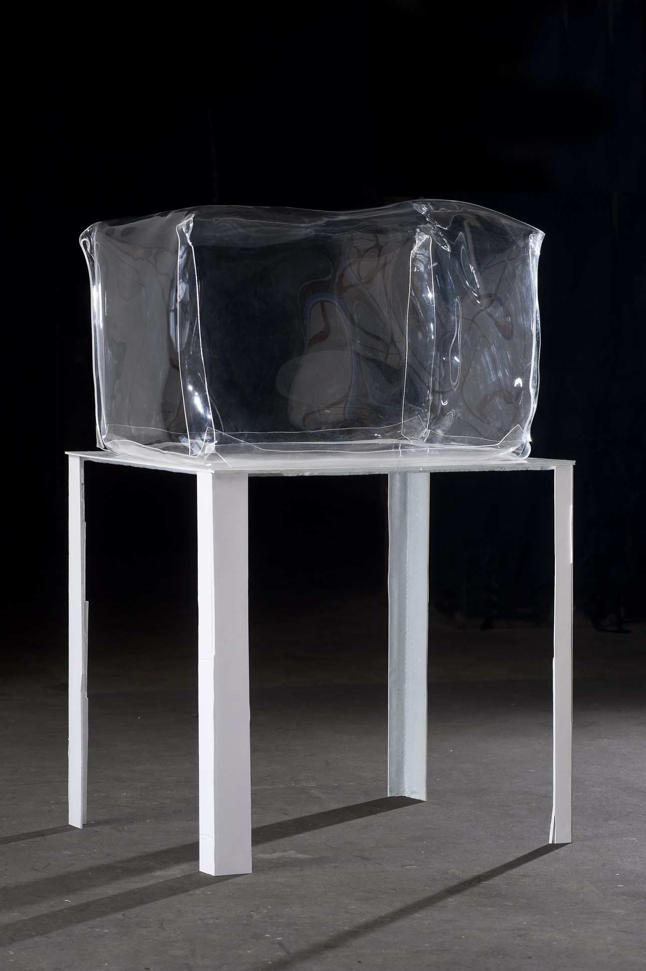 Clear acrylic sculptural work on white pedestal against dark background.