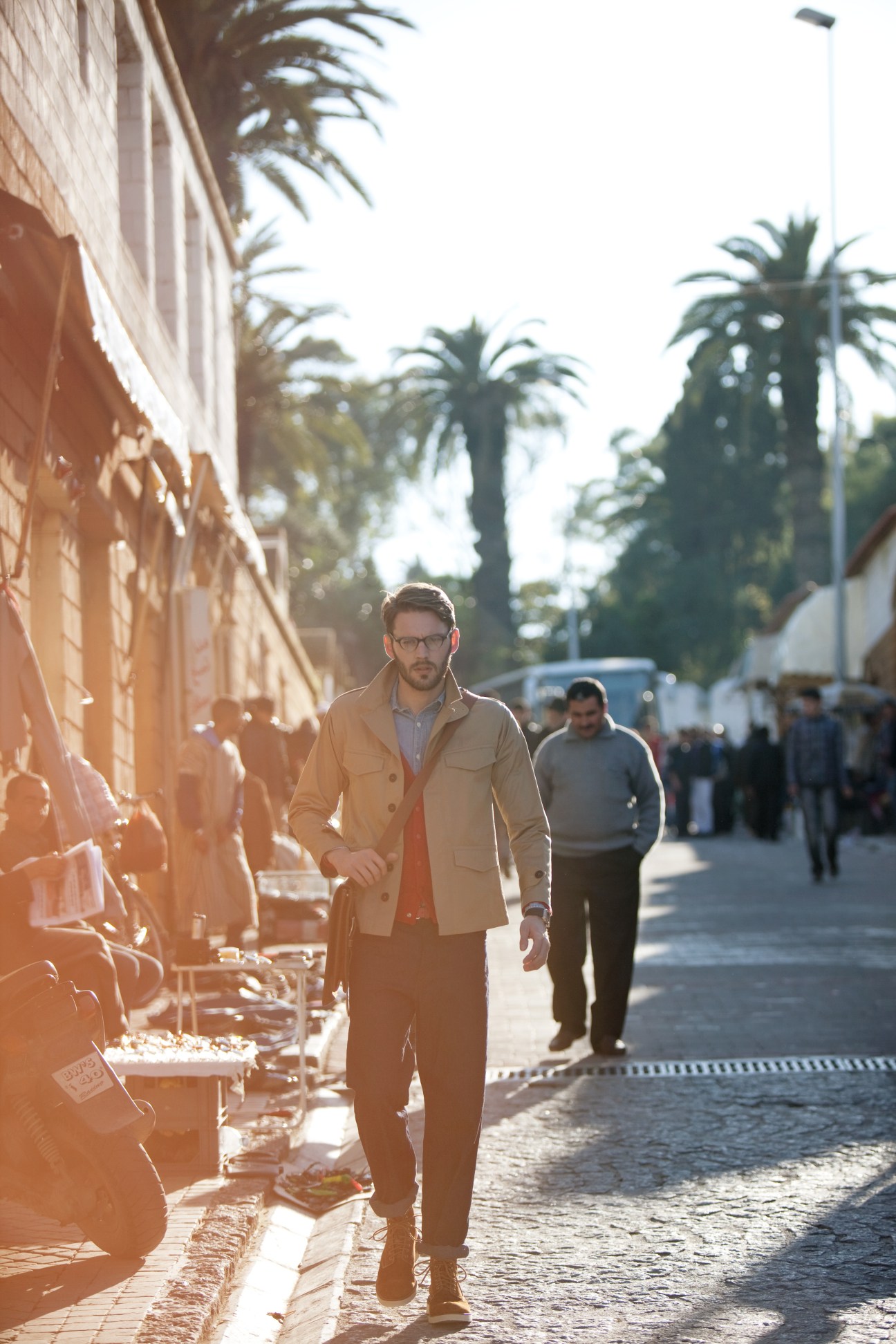 Man wearing A.P.C. jacket and cardigan with Oliver Spencer jeans walking in Tangier medina with palm trees.