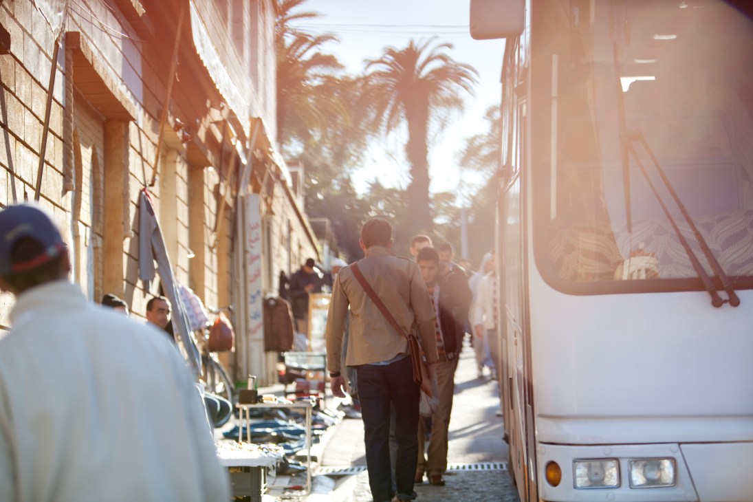 Man walking through sunlit Tangier medina street with palm trees and storefronts