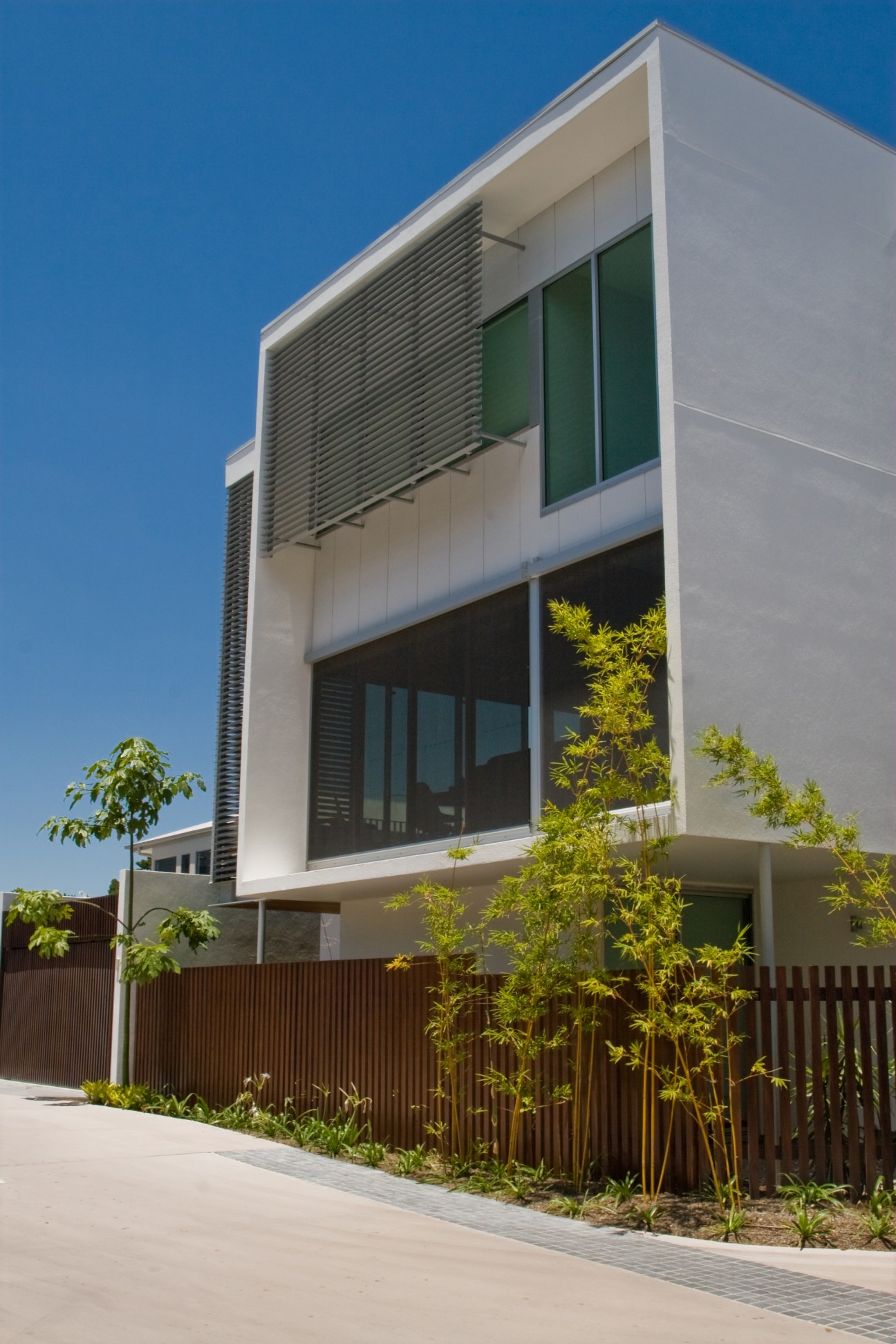 Modern white residential building with horizontal louvres, green windows, and timber fencing designed by BVN architects.