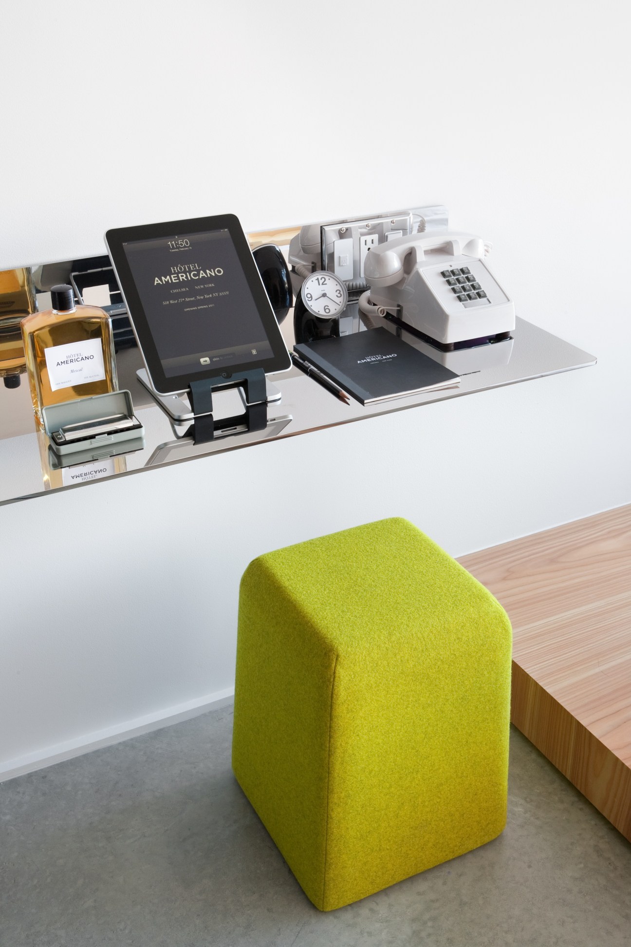 Hotel Americano in-room work station with tablet, phone, clock, and desk accessories on white desk with lime green stool.