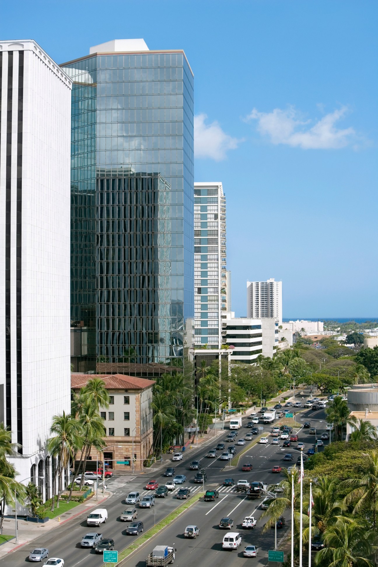 Busy urban street with modern high-rise buildings, palm trees, and heavy traffic congestion on a wide highway.