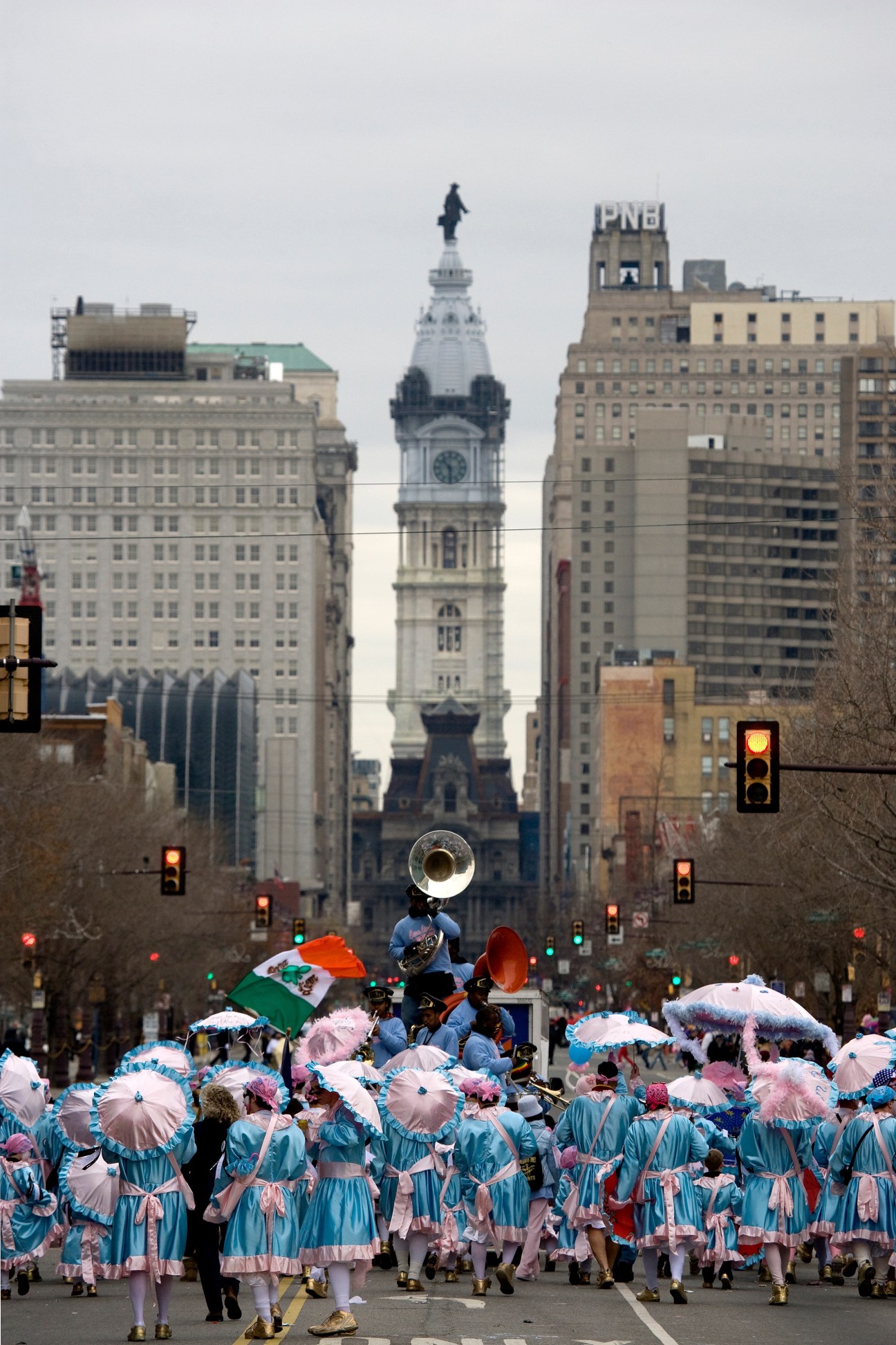 Parade participants in blue and pink costumes with umbrellas marching down a Philadelphia street towards City Hall.