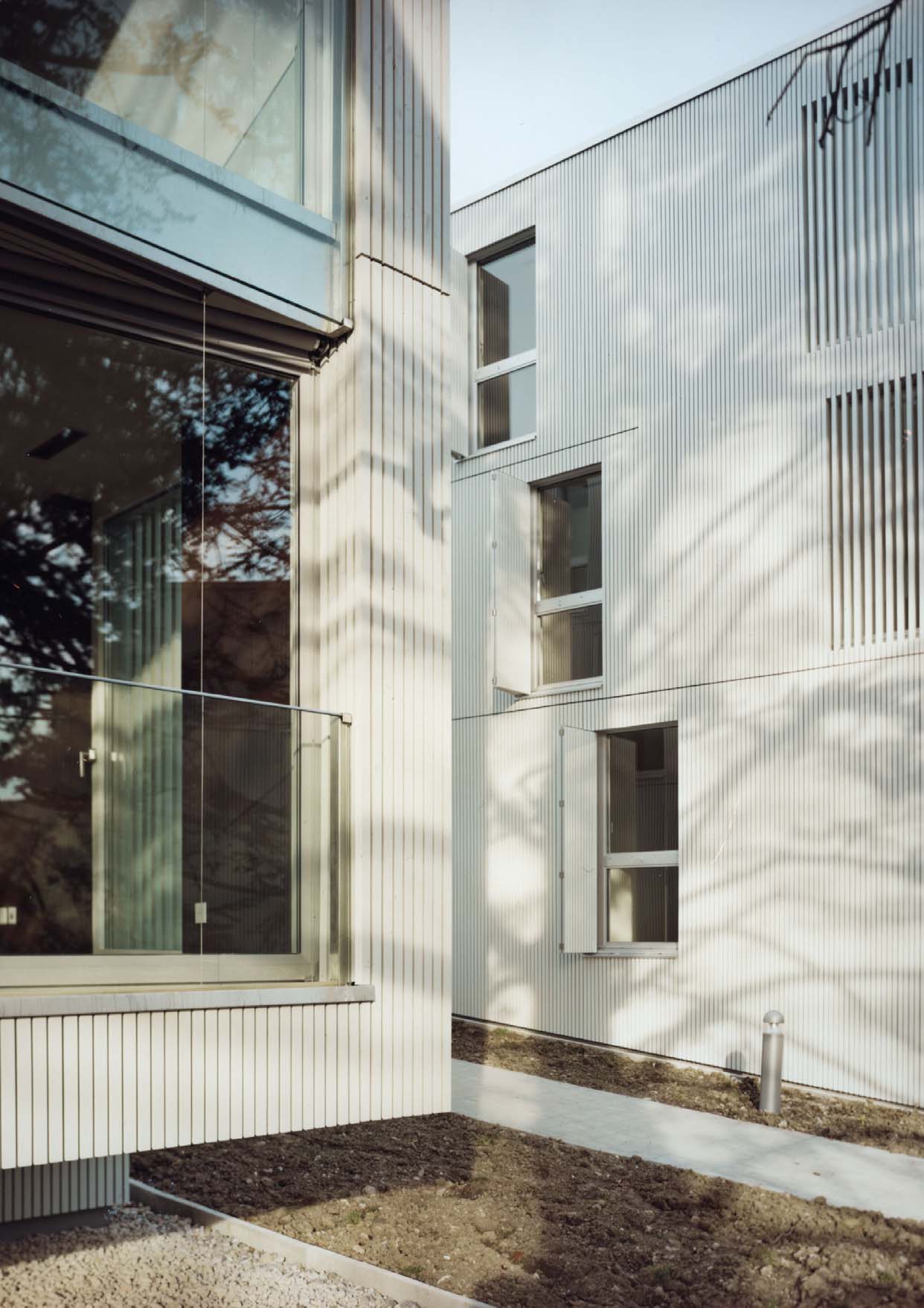 Modern white wooden apartment building with large glass windows and clean geometric facades beside a lake.