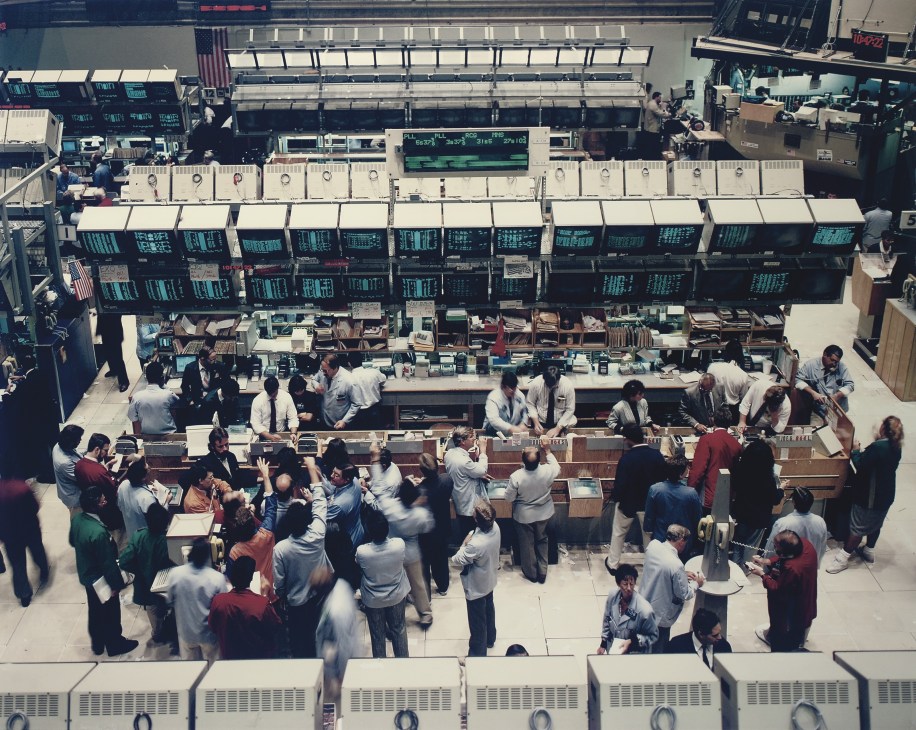 Aerial view of the New York Stock Exchange trading floor with rows of trading stations and crowds of traders.