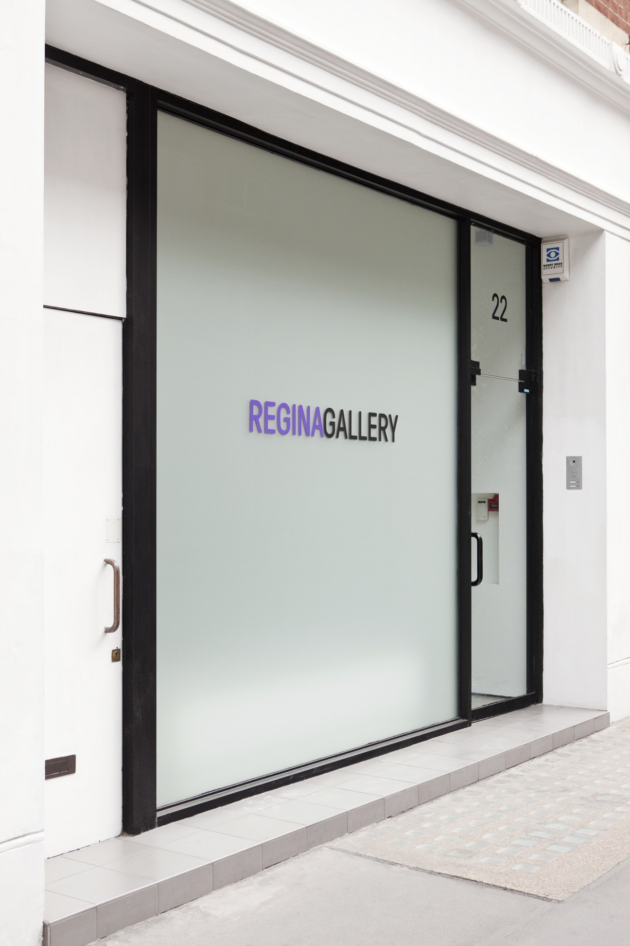 Storefront of Regina Gallery in London's Fitzrovia with black frames and frosted glass entrance at number 22.