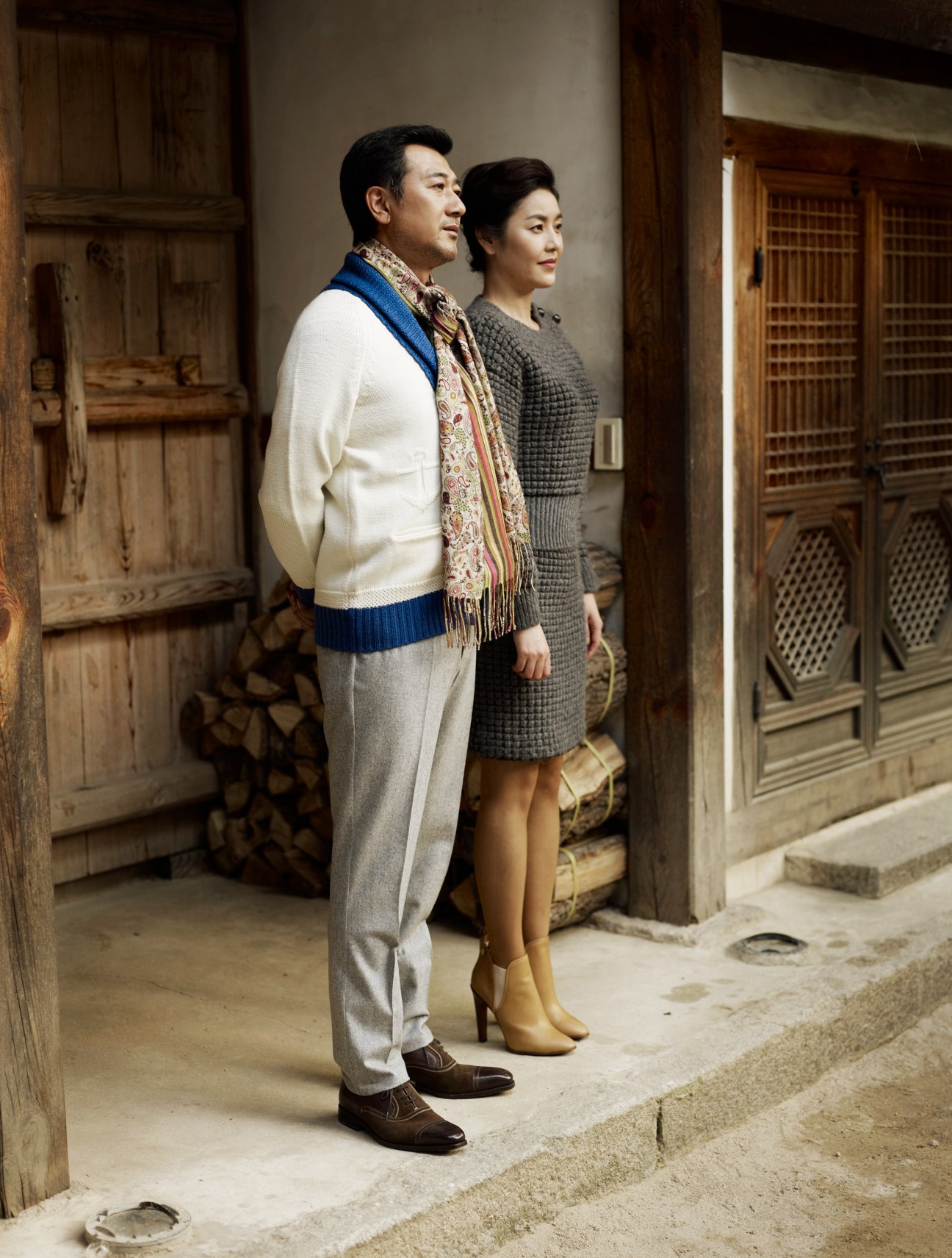 A man and woman stand together in a traditional Korean courtyard wearing coordinated smart casual outfits for Christmas.
