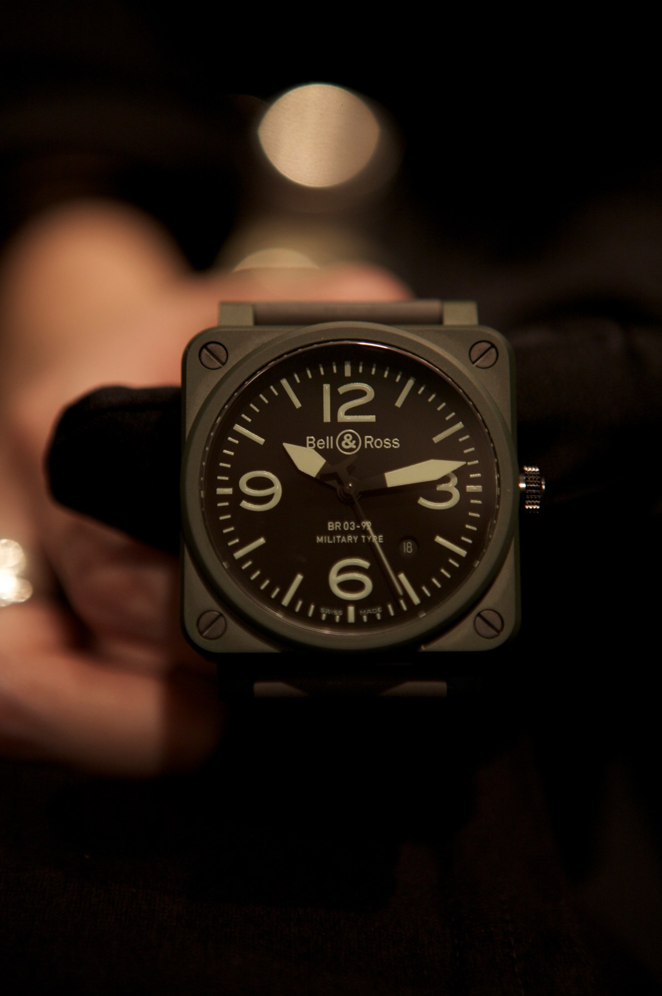 Bell & Ross BR 03-92 military-style watch with square ceramic case and luminescent dial held in hand.
