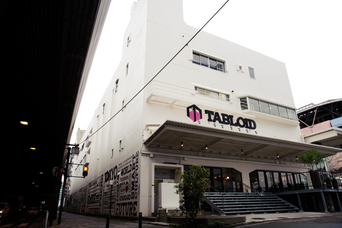 Exterior of Tabloid, a converted print factory in Tokyo with white facade and pink logo signage.
