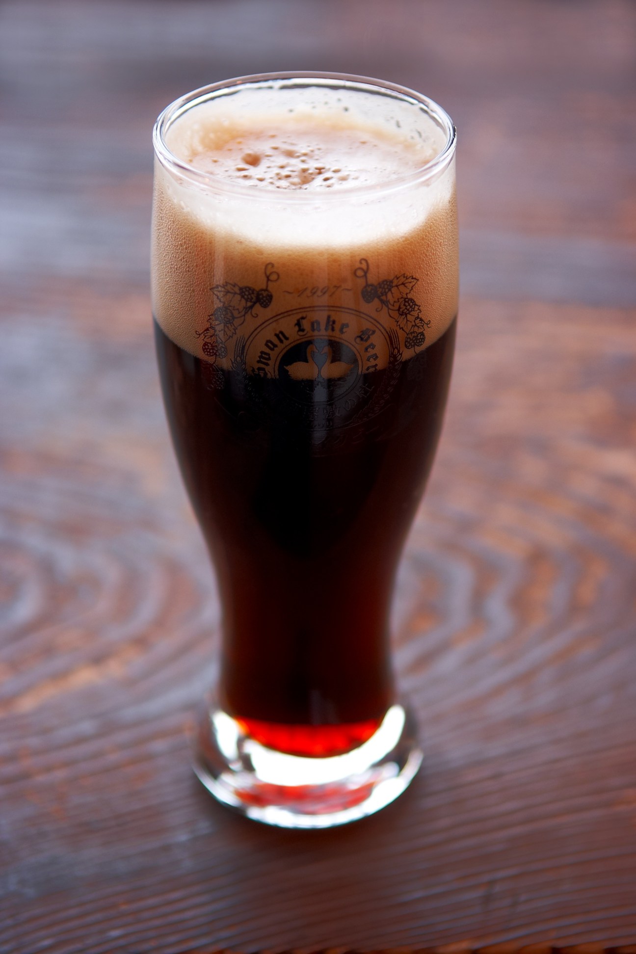 Glass of dark porter beer with creamy head and Swan Lake brewery logo on the glass