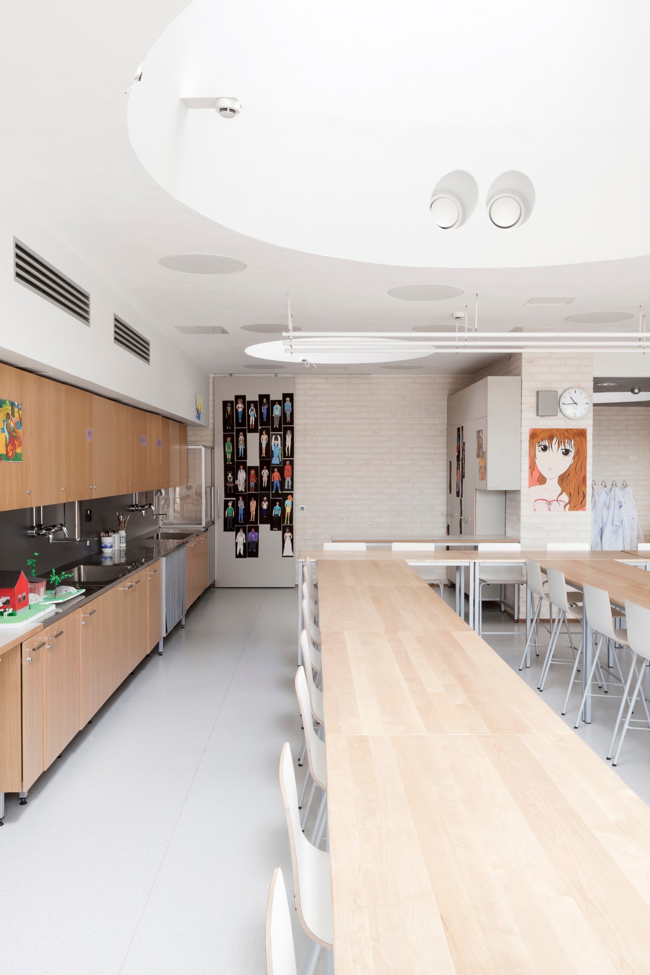 Modern art studio at Kirkkojärvi School with wooden cabinetry, white chairs, and curved white ceiling with skylights.