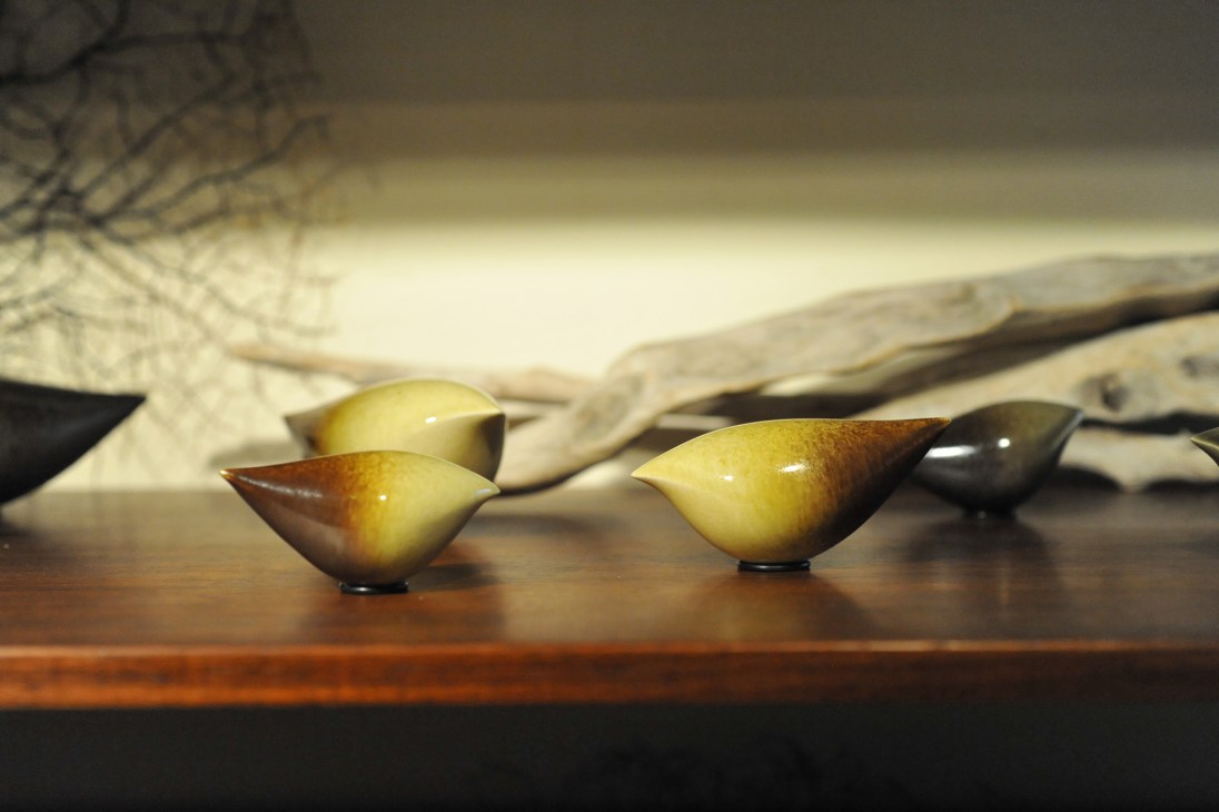 Yellow and brown ceramic bird sculptures displayed on a wooden surface with branches.