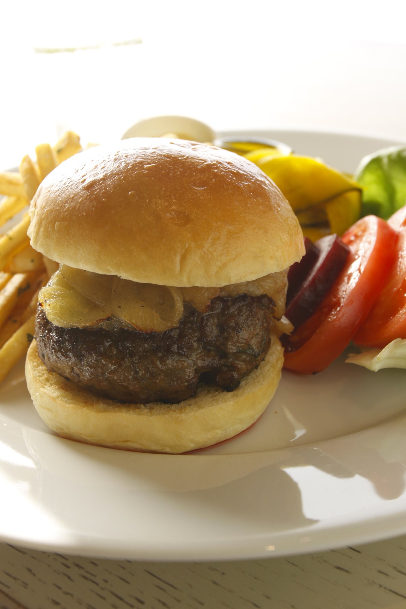 Burger with caramelized onions served with fries and roasted vegetables on white plate