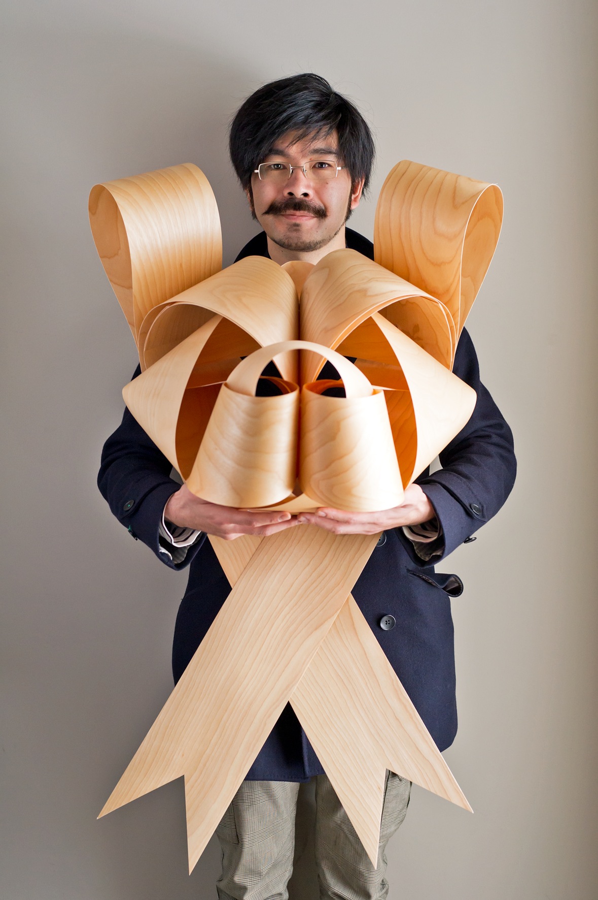 Man holding a wooden ribbon sculpture shaped like a lion's face.