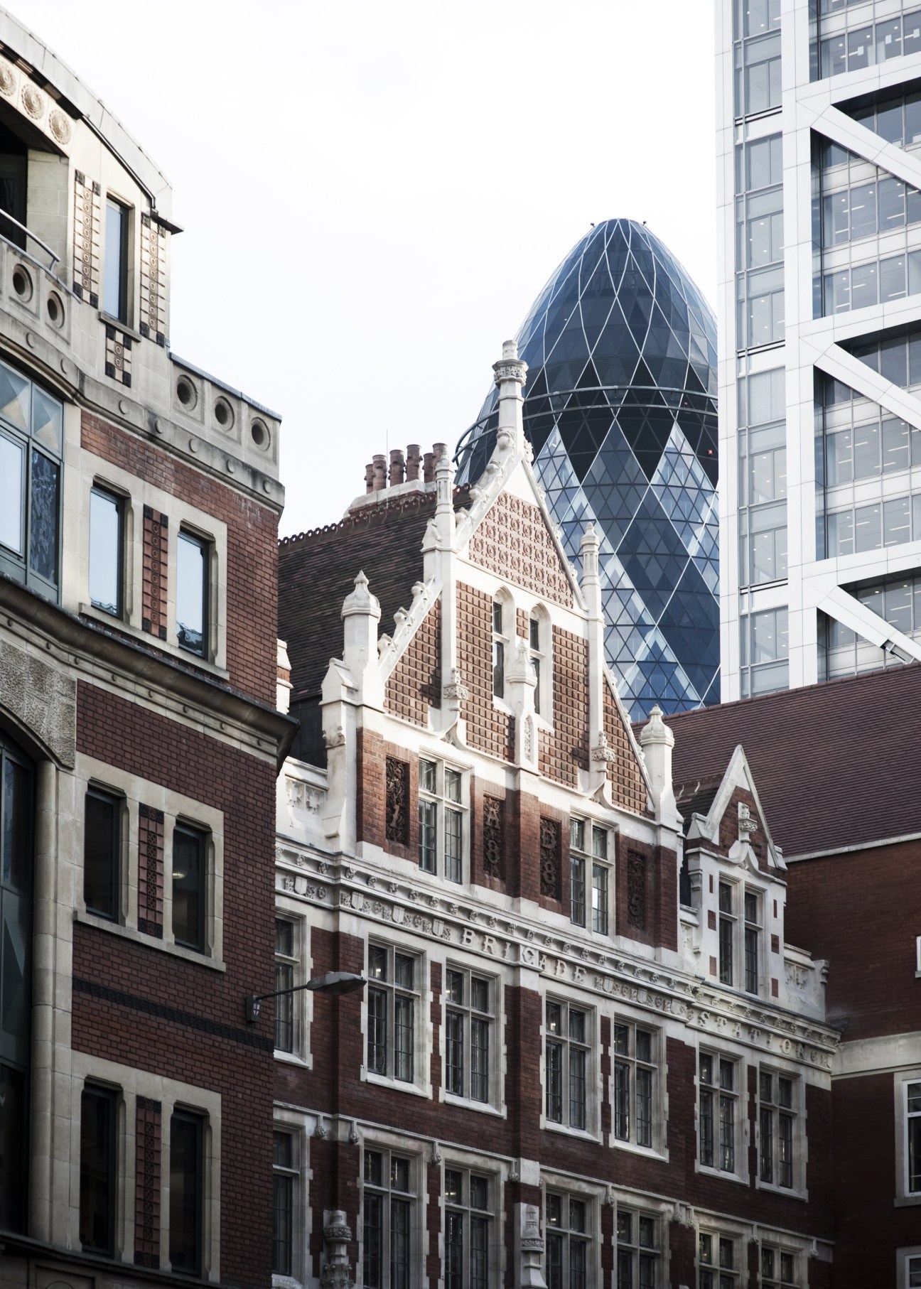Victorian brick building with ornate details and the modern Gherkin skyscraper rising behind it in London's Liverpool Street area.