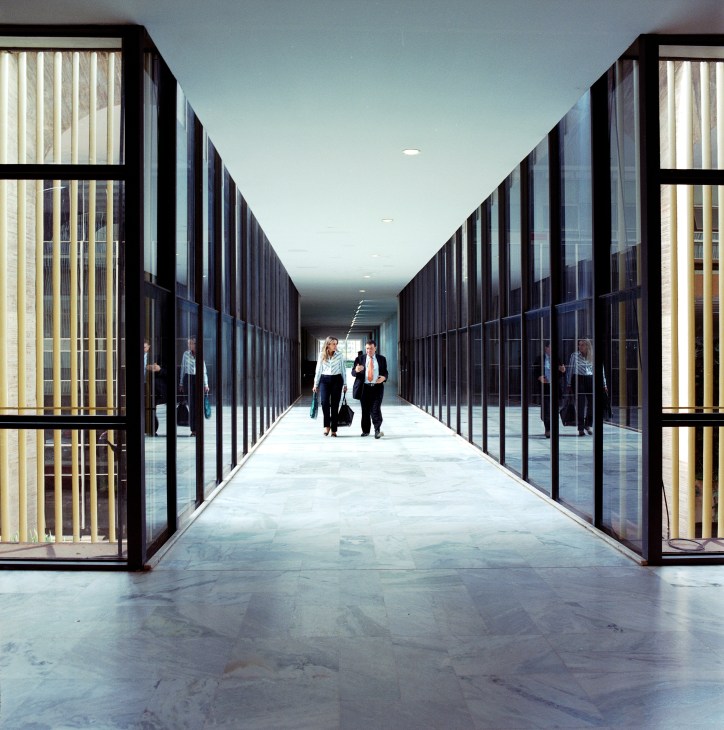 Modern corridor with symmetrical glass and black metal doors on either side, polished marble floor, people walking in distance.