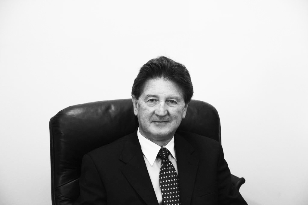 Edward Turner, director of Austasia airline, seated in black leather chair wearing dark suit and polka dot tie.