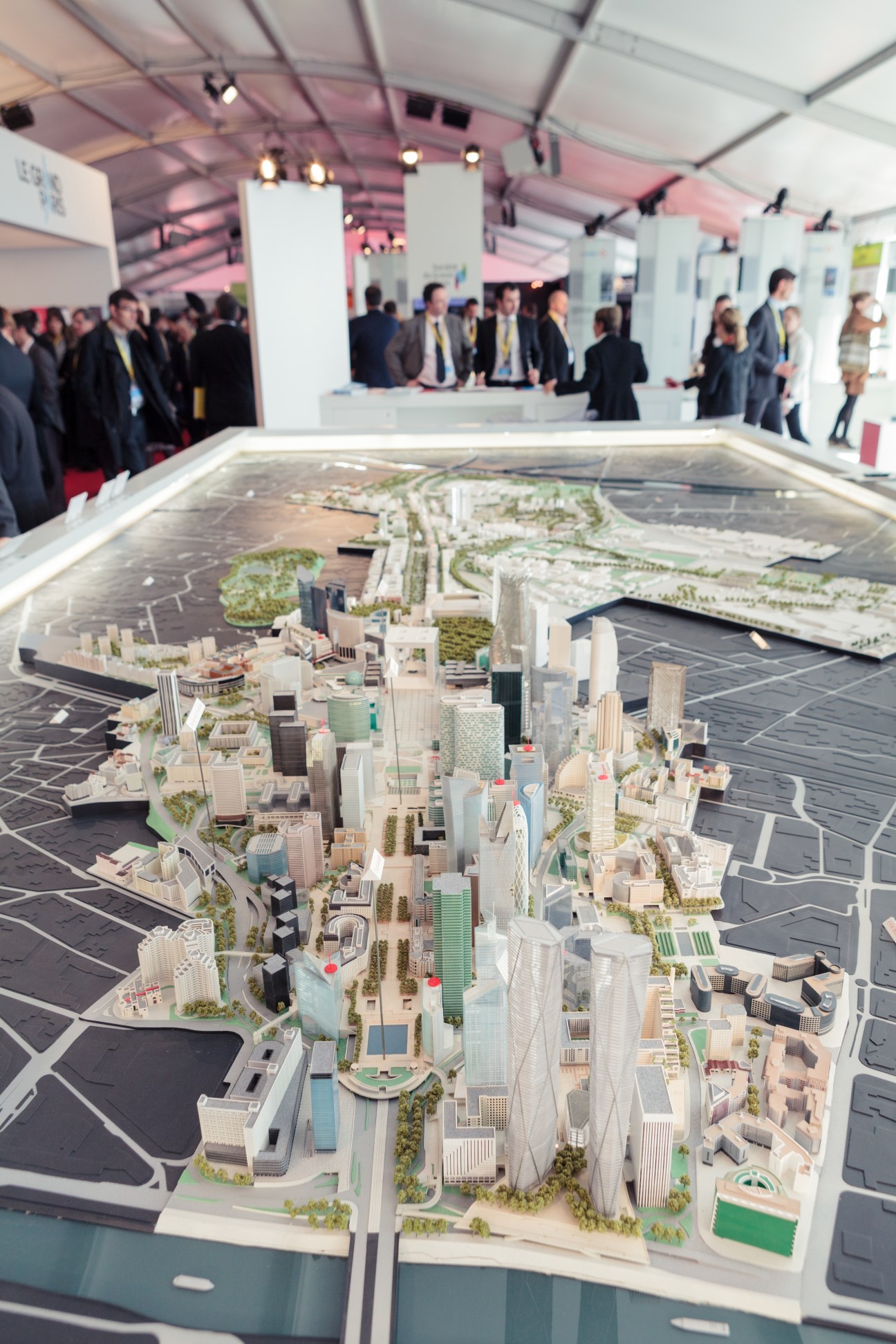 Architectural model of Paris development displayed at MIPIM booth with visitors in background.