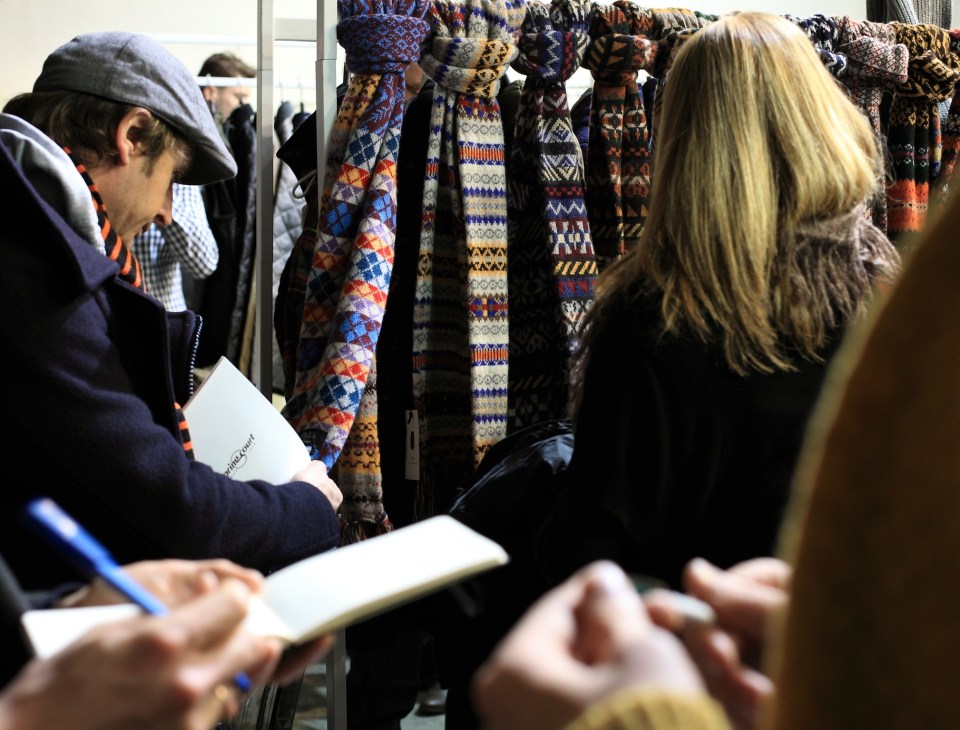Visitors examining Morrison Fair Isle knitwear displayed on hangers at a trade fair.