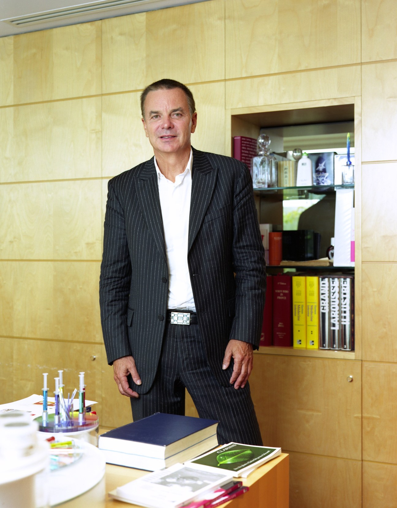 Dr Olivier Courtin-Clarins stands in an office with wooden paneling and shelves of Clarins products behind him.