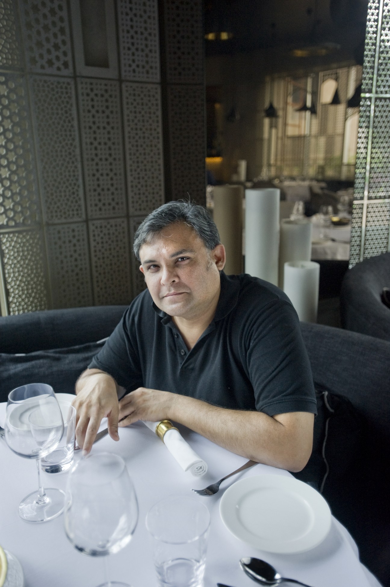 Marut Sikka sits at a white dining table at his restaurant Kainoosh, wearing a black polo shirt.