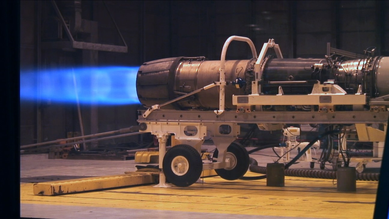 F/A-18 aircraft engine being tested to run on biofuel, emitting bright blue flame during test.