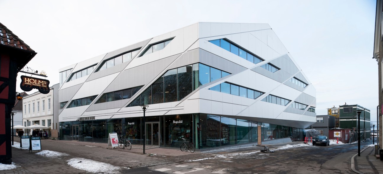 Modern white building with curved architectural lines and large windows, featuring ground-floor retail spaces and bicycles parked outside.