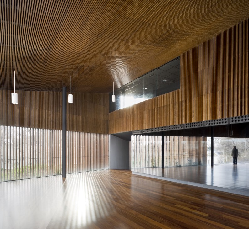 Interior of Environmental Department Building in Zaragoza with wood-paneled walls, pendant lights, and panoramic windows overlooking landscape.