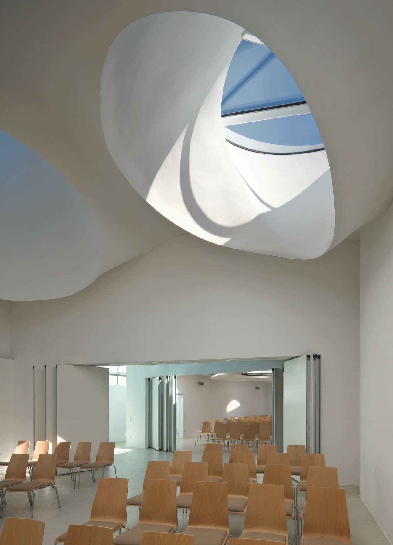 Interior of Martin Luther Church in Hainburg, Austria, designed by Coop Himmelb(l)au, featuring twisted steel roof structure and angled skylight openings.