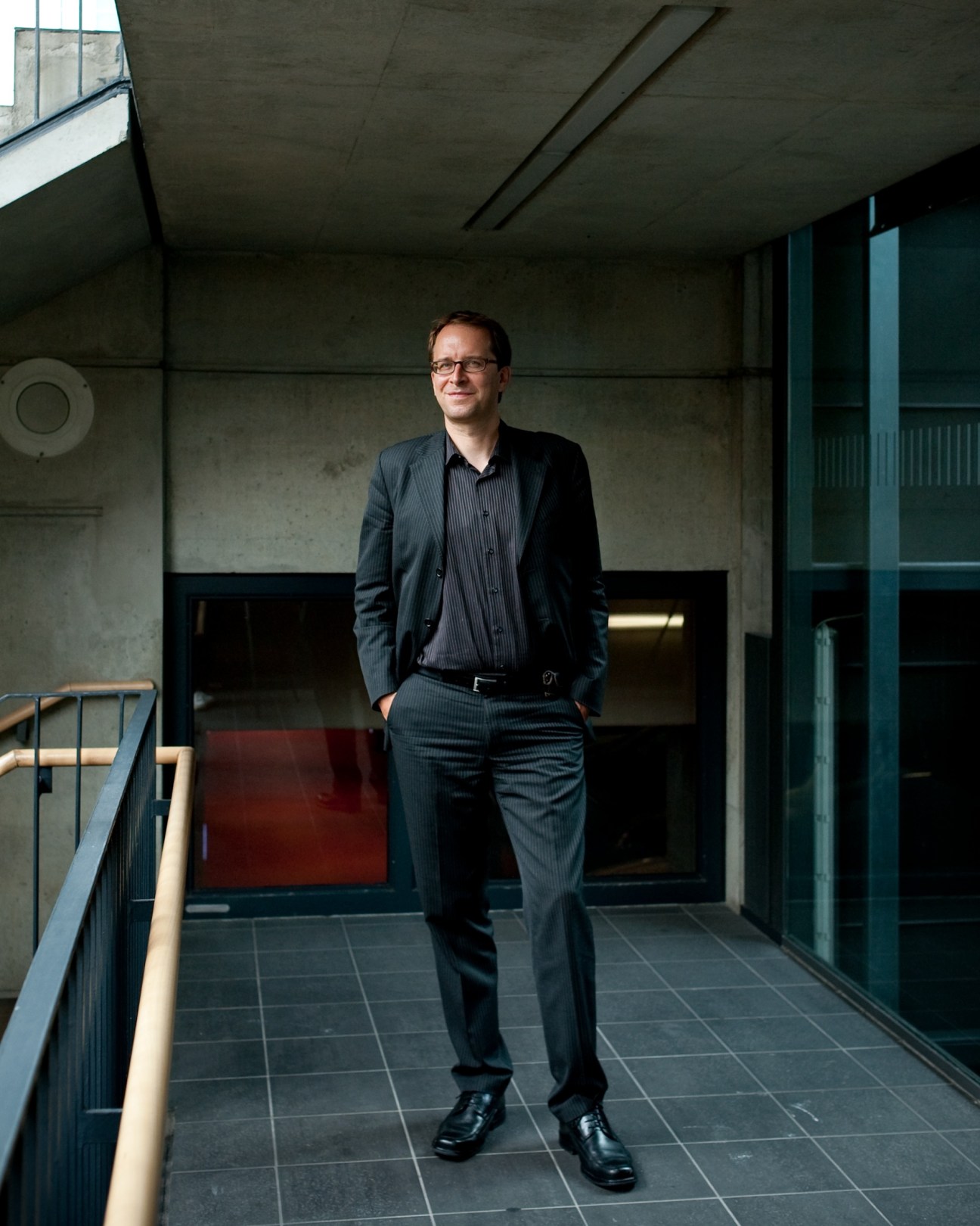 Andreas Leo, Daimler spokesman, standing in a modern concrete corridor wearing a dark pinstriped suit.