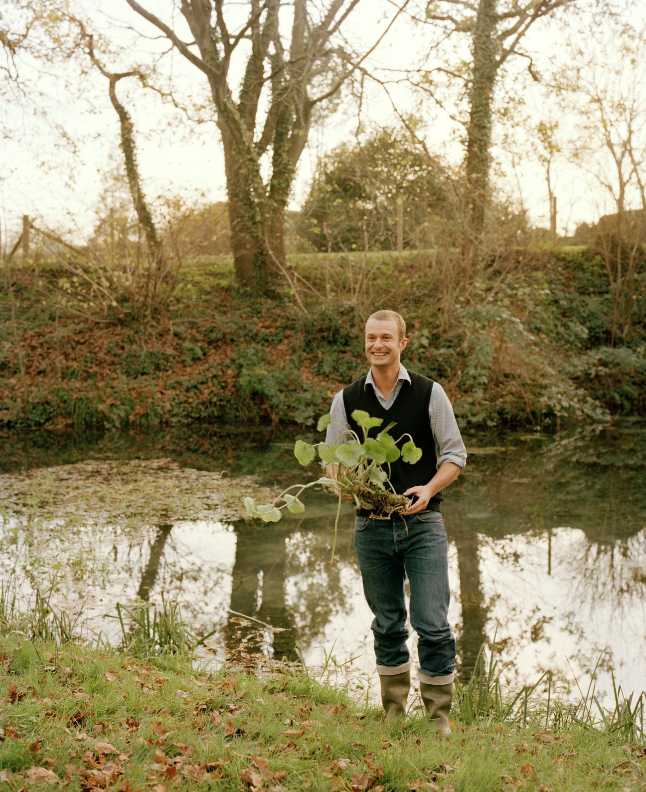 James Harper, product manager for The Wasabi Company, holding a wasabi plant by water in Dorset.