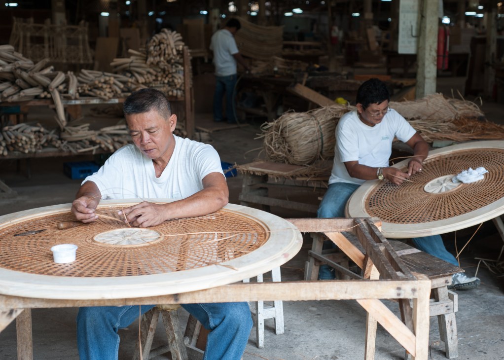 Two Filipino craftsmen weave rattan furniture at a workshop in Cebu.